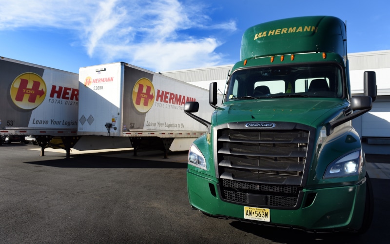 a close up of a green truck facing the camera with two white and gray trailers parked behind it