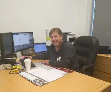 a person sitting at a table with a laptop and smiling at the camera