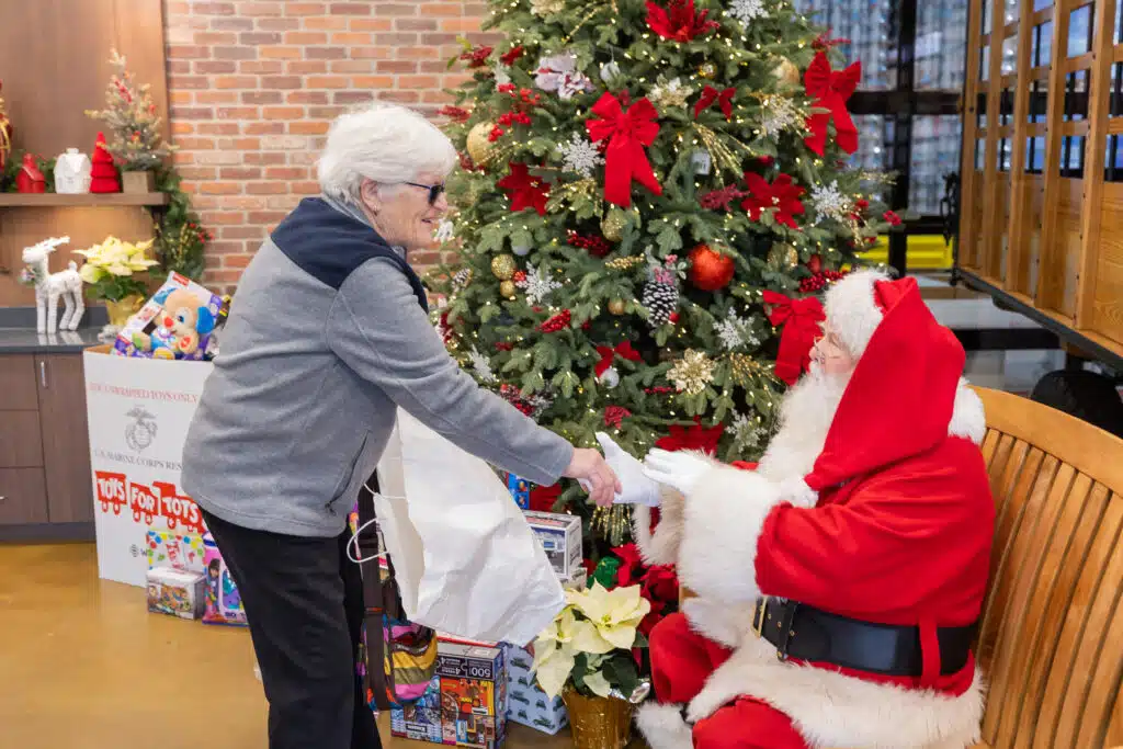 a smiling old woman holds hands with Santa Claus who sits on a wooden bench